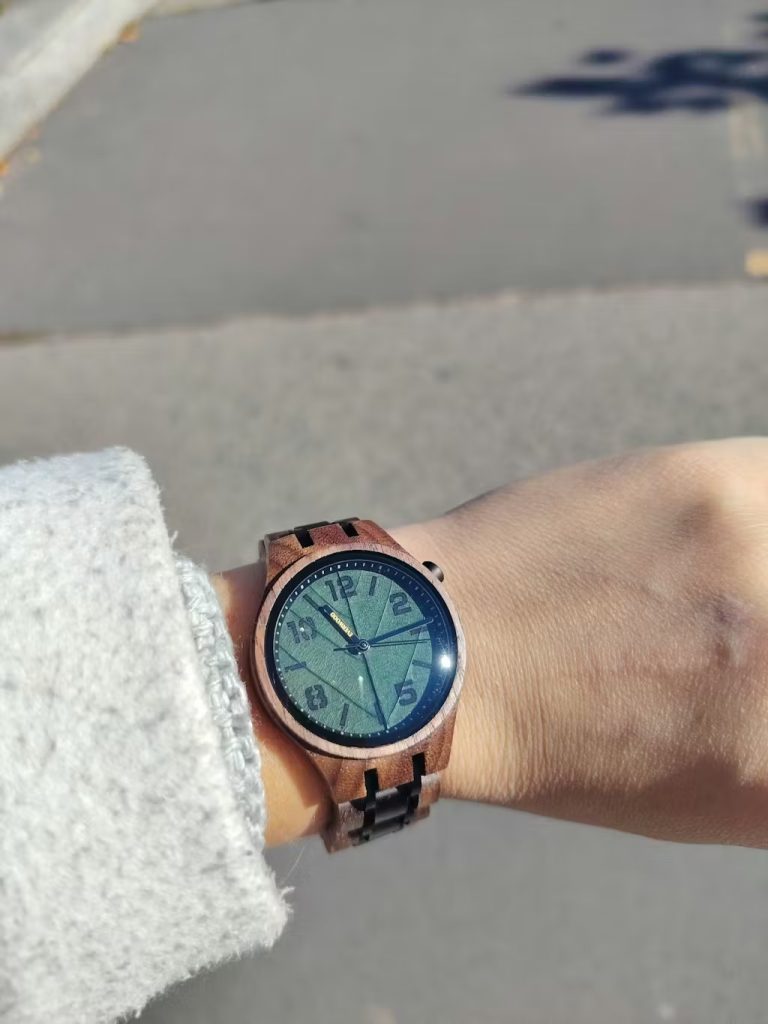 Fotósorozat, amely az EverWood óra viselését szemlélteti: egy női kéz eukaliptusz ágat tart az óra mellett, egy közeli kép a számlapról, és egy kép, ahol az óra egy zöld ingujjal és fűvel a háttérben látszik